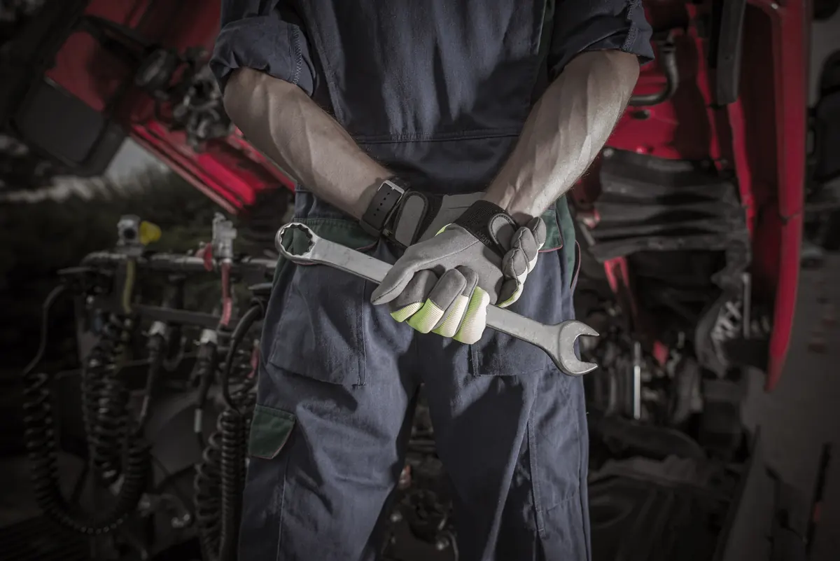 ALMO diesel technician holding spanners in front of a truck engine